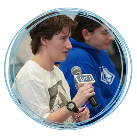 A student holding a microphone asks a question at a U N E event