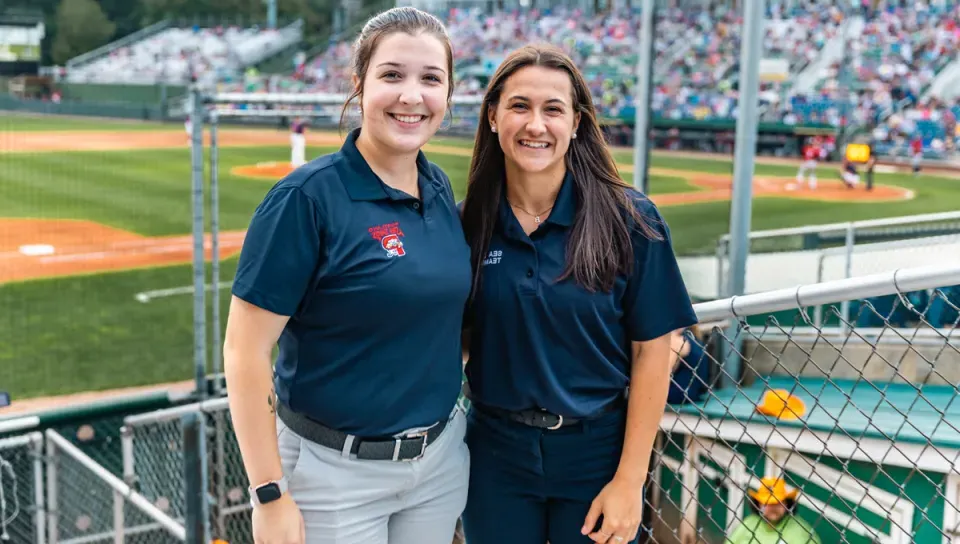 Two students wearing Sea Dogs polo navy shirts stand in front of Hadlock Field